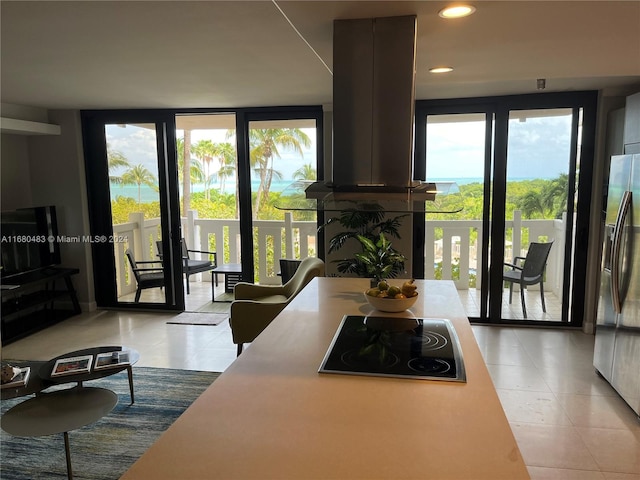 kitchen with island range hood, black electric cooktop, stainless steel fridge with ice dispenser, light tile patterned floors, and expansive windows