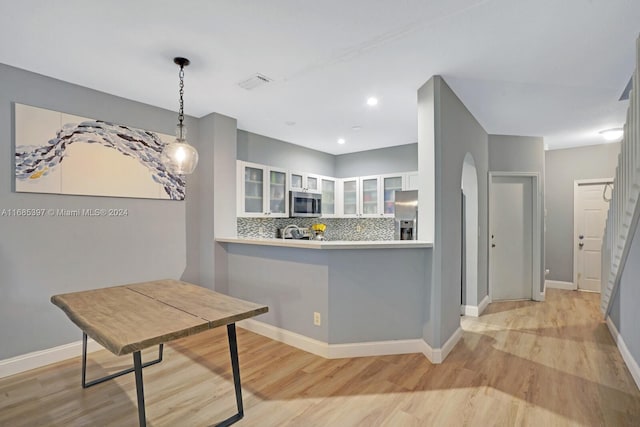 kitchen with hanging light fixtures, kitchen peninsula, backsplash, white cabinetry, and appliances with stainless steel finishes