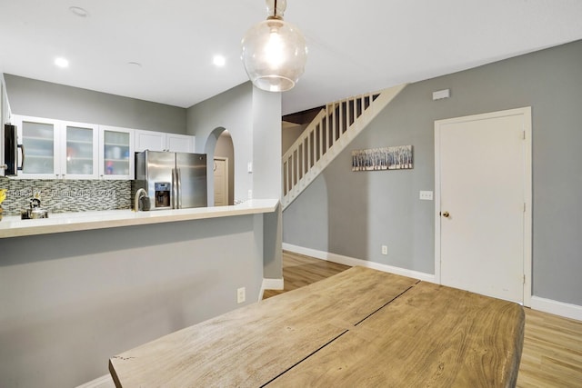 kitchen featuring decorative backsplash, light hardwood / wood-style flooring, stainless steel fridge with ice dispenser, pendant lighting, and white cabinets