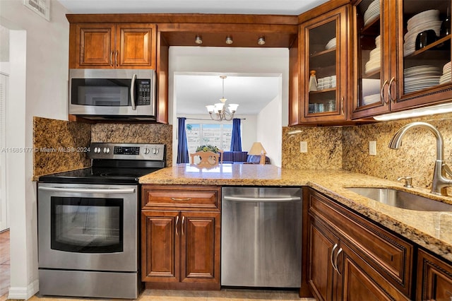 kitchen featuring light stone countertops, sink, stainless steel appliances, decorative backsplash, and a chandelier