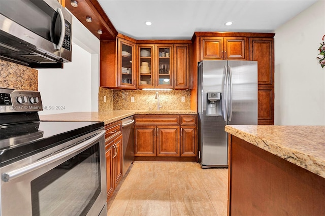 kitchen featuring appliances with stainless steel finishes, sink, light stone counters, decorative backsplash, and light tile patterned floors