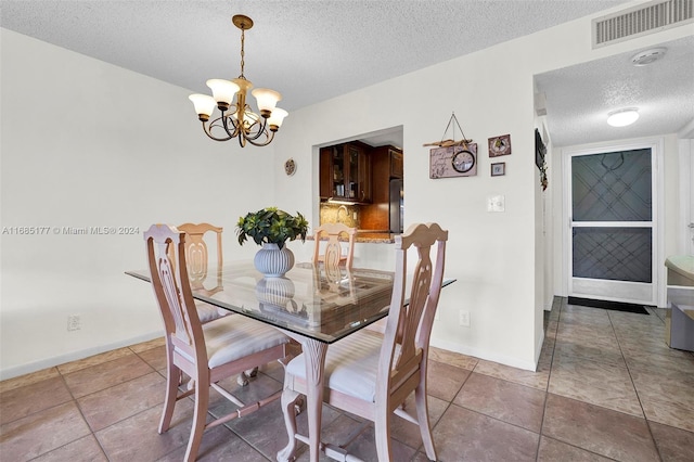 dining space with a textured ceiling, a chandelier, and tile patterned flooring