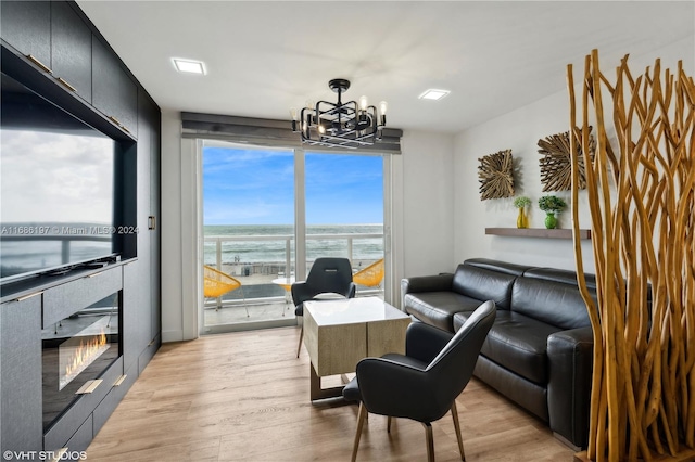 living room with a chandelier, a tiled fireplace, a water view, and light hardwood / wood-style floors