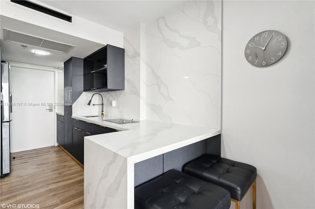 kitchen featuring black electric stovetop, decorative backsplash, sink, light stone countertops, and light hardwood / wood-style floors