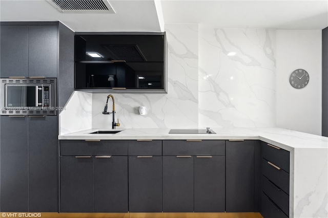 kitchen featuring black electric stovetop, light stone countertops, sink, stainless steel microwave, and decorative backsplash