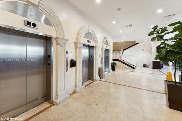 hallway with a towering ceiling, elevator, and ornate columns