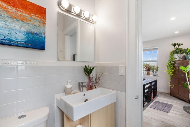 bathroom featuring toilet, recessed lighting, wood finished floors, a sink, and tile walls