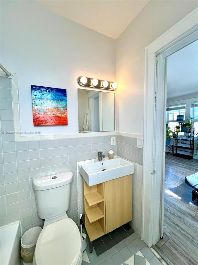 bathroom with toilet, wainscoting, vanity, and tile walls