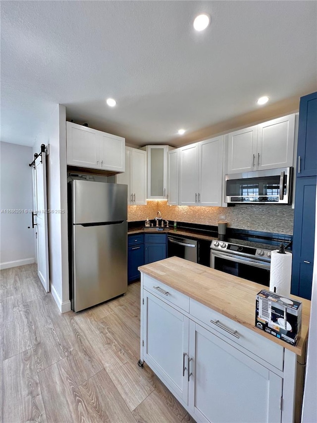 kitchen featuring white cabinets, decorative backsplash, butcher block countertops, appliances with stainless steel finishes, and blue cabinetry