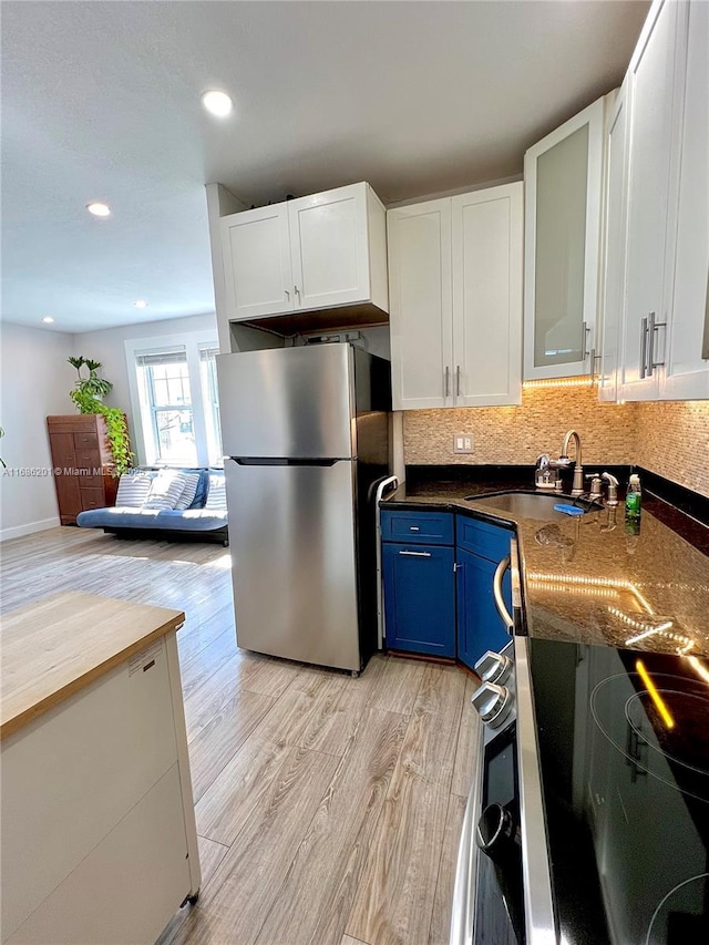 kitchen featuring light wood finished floors, freestanding refrigerator, blue cabinetry, white cabinetry, and a sink