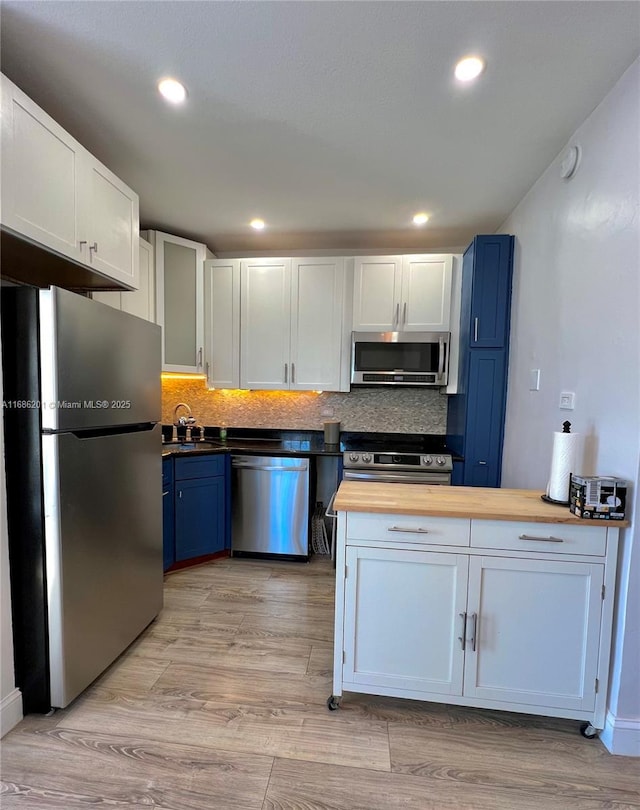 kitchen featuring tasteful backsplash, light wood-style floors, stainless steel appliances, blue cabinetry, and wooden counters