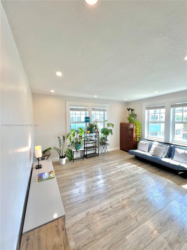 living room featuring light wood-style floors, plenty of natural light, baseboards, and a textured ceiling