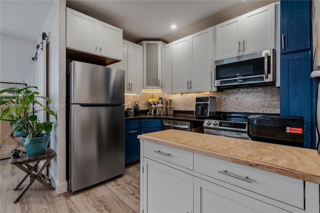 kitchen featuring stainless steel appliances, blue cabinetry, white cabinets, light hardwood / wood-style floors, and tasteful backsplash