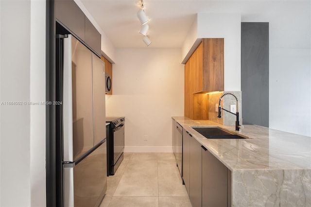 kitchen with track lighting, sink, light tile patterned floors, appliances with stainless steel finishes, and light stone counters