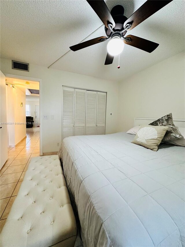 tiled bedroom featuring ceiling fan, a textured ceiling, and a closet