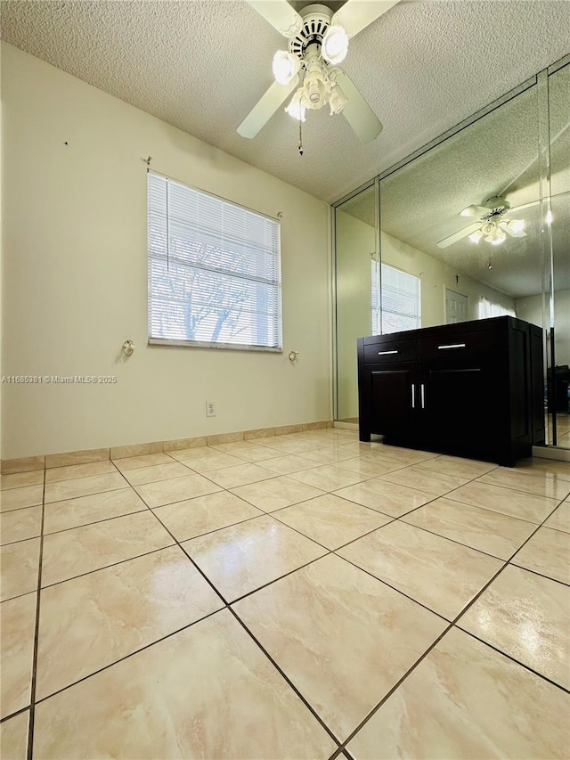 tiled empty room featuring ceiling fan and a textured ceiling