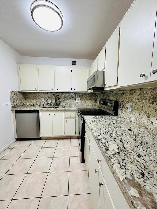 kitchen featuring appliances with stainless steel finishes, white cabinetry, sink, backsplash, and light tile patterned flooring