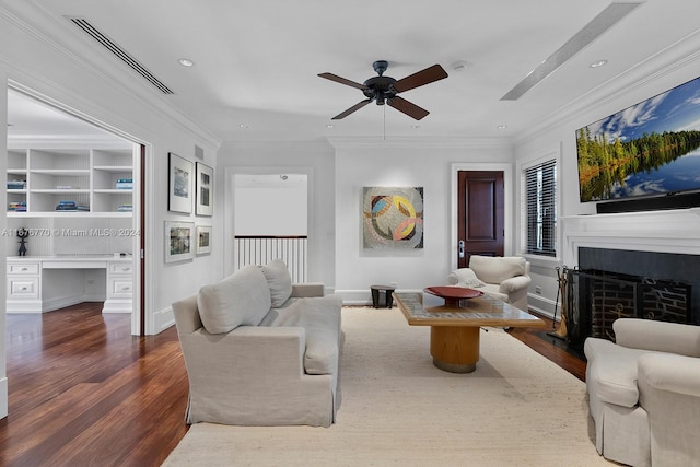 living room with built in desk, ceiling fan, dark wood-type flooring, and ornamental molding