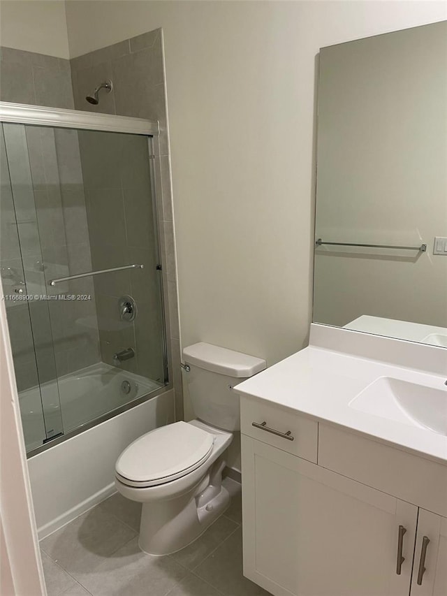 full bathroom with combined bath / shower with glass door, vanity, tile patterned flooring, and toilet