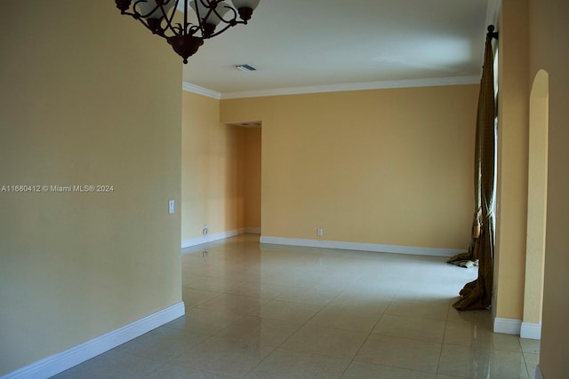 empty room with crown molding, light tile patterned floors, and a notable chandelier