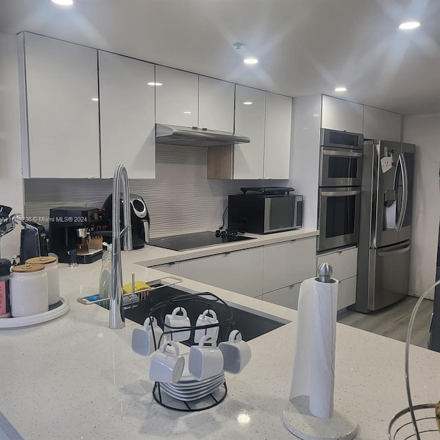 kitchen featuring decorative backsplash, light hardwood / wood-style flooring, stainless steel appliances, white cabinetry, and light stone counters