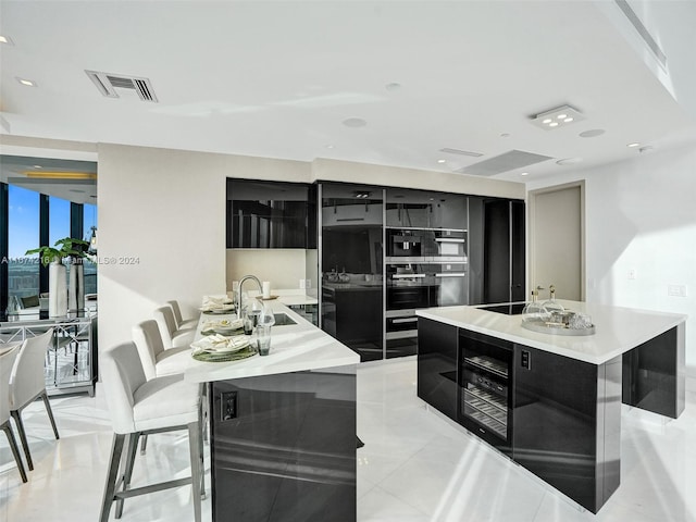 kitchen with a breakfast bar area, an island with sink, wine cooler, light tile patterned flooring, and black double oven