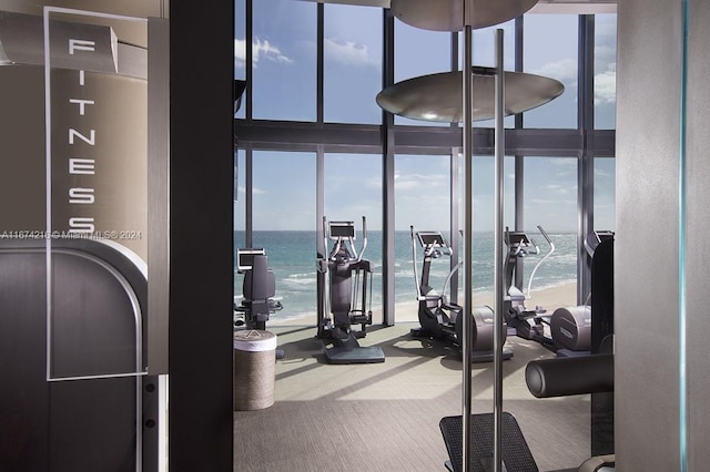 workout area with a water view, carpet flooring, expansive windows, and a beach view