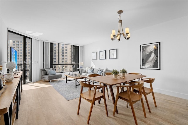 dining area with light hardwood / wood-style floors, a wall of windows, a chandelier, and a skylight