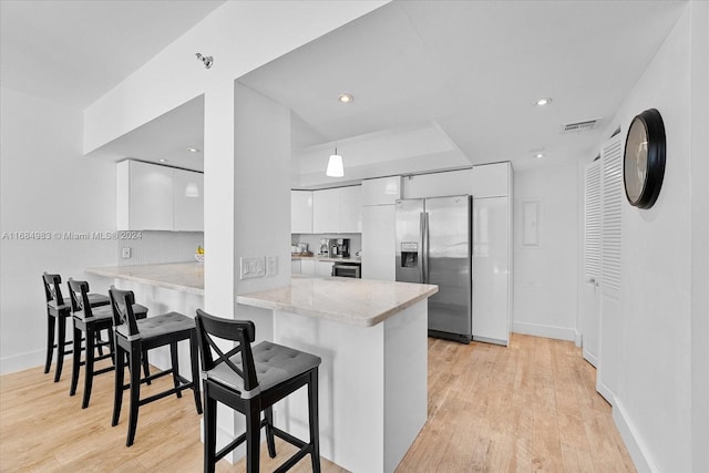 kitchen with kitchen peninsula, stainless steel fridge, white cabinetry, a kitchen bar, and light hardwood / wood-style floors