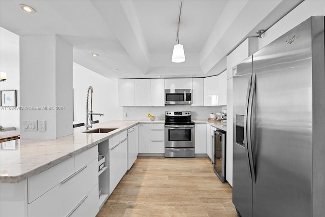 kitchen with hanging light fixtures, kitchen peninsula, stainless steel appliances, white cabinetry, and light hardwood / wood-style floors