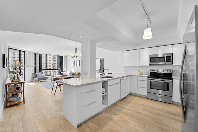 kitchen with stainless steel appliances, hanging light fixtures, light wood-type flooring, and white cabinets