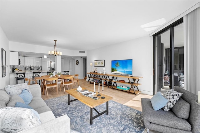 living room featuring a notable chandelier, a skylight, and light wood-type flooring