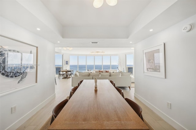 dining room featuring light hardwood / wood-style floors, an inviting chandelier, a raised ceiling, and a water view