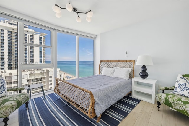 bedroom with wood-type flooring, a water view, and a wall of windows