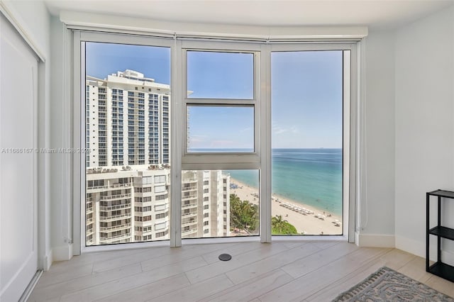 doorway to outside with a view of the beach, a water view, a healthy amount of sunlight, and light wood-type flooring