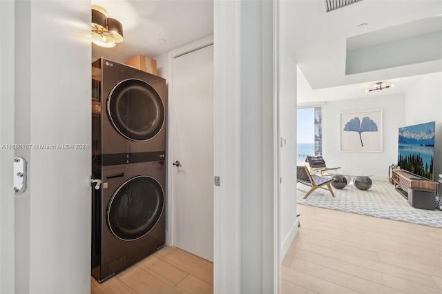 laundry room with light wood-type flooring and stacked washer / drying machine