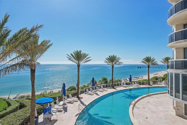 view of swimming pool featuring a beach view, a water view, and a patio