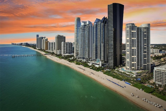 aerial view at dusk featuring a view of the beach and a water view