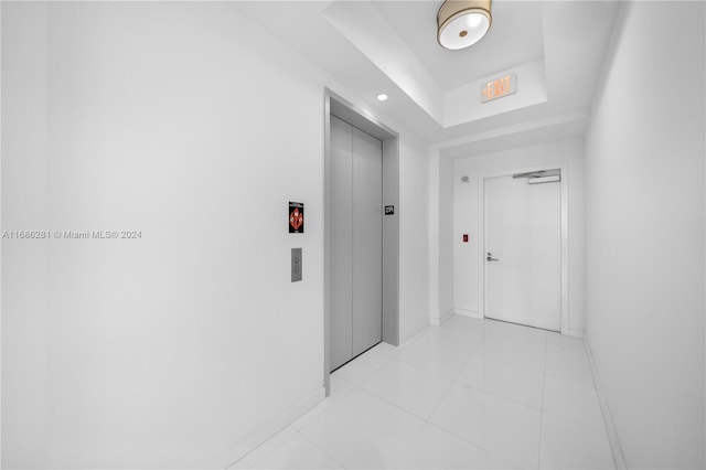 corridor with a raised ceiling, elevator, and light tile patterned flooring