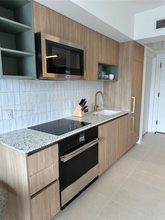 kitchen with light stone countertops, sink, backsplash, and appliances with stainless steel finishes