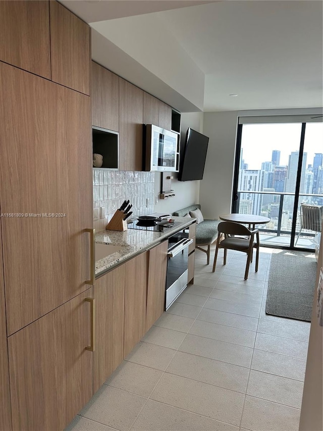 kitchen featuring light stone countertops, appliances with stainless steel finishes, backsplash, and light tile patterned flooring