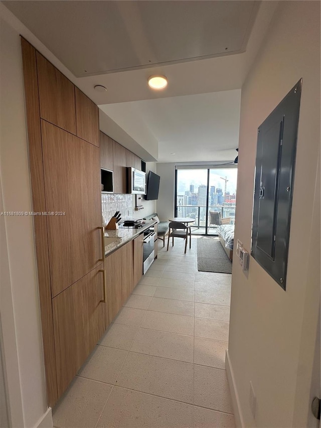 kitchen featuring stainless steel appliances, floor to ceiling windows, light stone countertops, backsplash, and electric panel