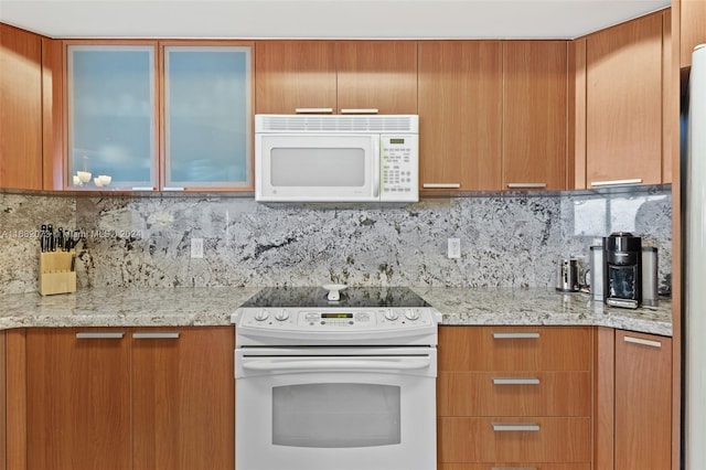 16699 Collins Ave Unit 2202, Sunny Isles Beach, FL 33160 - kitchen featuring white appliances, glass insert cabinets, decorative backsplash, and brown cabinetry