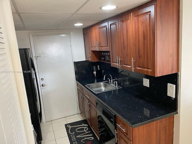 kitchen featuring dishwasher, black refrigerator, sink, light tile patterned floors, and a paneled ceiling