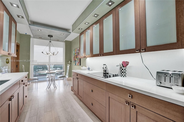 kitchen with a notable chandelier, light hardwood / wood-style flooring, black electric cooktop, and hanging light fixtures