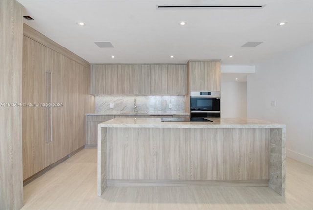 kitchen with a spacious island, sink, light brown cabinets, and light hardwood / wood-style flooring