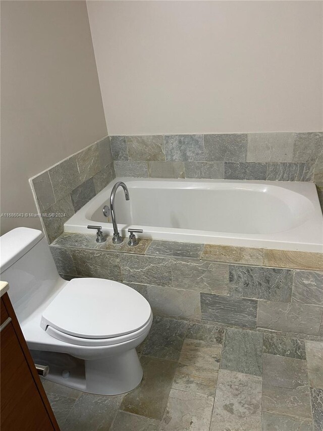 bathroom with vanity, toilet, and tiled bath