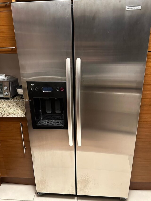 details with light stone countertops, stainless steel fridge with ice dispenser, and light tile patterned floors