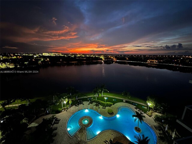 pool at dusk with a patio area and a water view