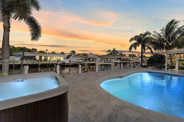 pool at dusk featuring a patio area, a hot tub, and a water view